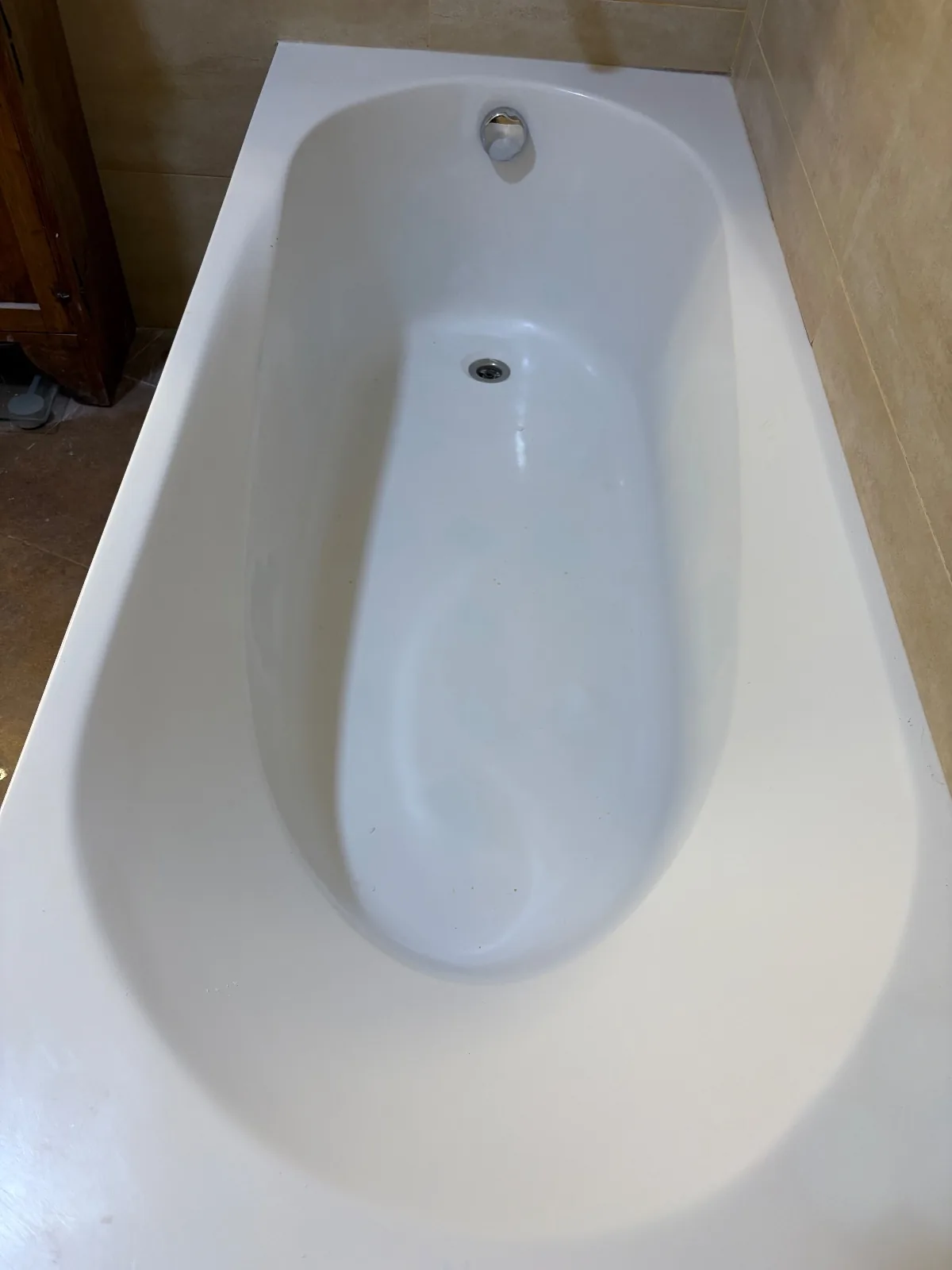 Bañera blanca de acabado brillante y uniforme junto a pared de azulejos beige